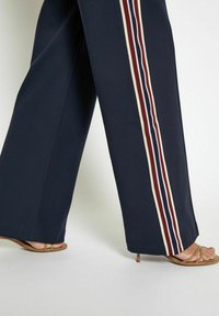 Navy wide-leg pants with vertical striped accents in cream, maroon, and red. Fabric appears smooth; paired with tan strappy sandals.
