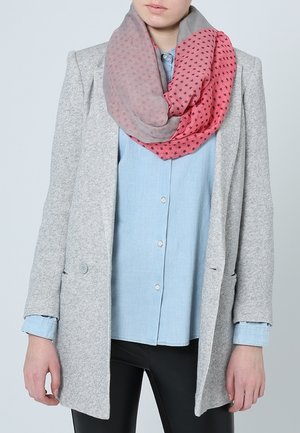 Femme portant un blazer gris, une chemise bleu clair à boutons, un pantalon noir et une écharpe infinie rose et grise à motif d'étoiles.