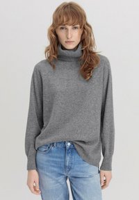 Grijze coltrui van zacht breiwerk, met lange mouwen en een relaxte pasvorm, gecombineerd met lichtblauwe jeans.