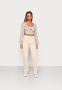 Top curto floral com mangas bufantes longas, apresentando um detalhe em forma de olho-chave; combinado com calças de perna reta em bege claro e sapatos brancos.