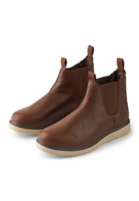 Botas de cuero marrón hasta el tobillo con paneles elásticos a los lados, trabillas y una suela de goma beige en contraste. Presenta detalles de costura alrededor de la suela.