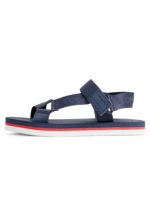 Navy blue open-toe sandal with adjustable straps, white sole with red stripe, and "Tommy Jeans" branding on the side strap.