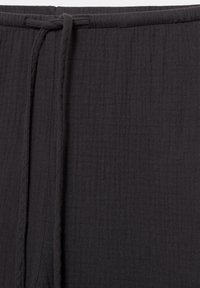 Gros plan d'un tissu noir texturé avec une couture cousue et une bande de tissu attachée verticalement.