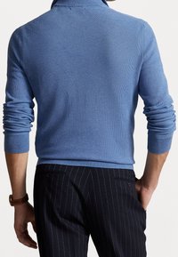 Blå, texturerad tröja med hög krage, med långa ärmar. Kombinerad med mörka randiga byxor.