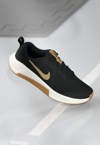 Fekete sportcipő textúrált felsőrésszel, arany Nike logóval és párnázott fehér talppal. Felszerelt fűzőkkel és egy húzófüllel a sarkán.