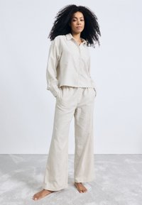 Lichtbeige linnen loungewear set met een gecropt knoopshirt en brede broek, met een relaxte pasvorm en minimale naden.