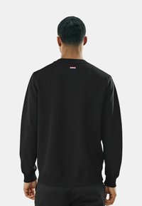 Felpa nera con scollo rotondo, maniche lunghe e un accento tricolore orizzontale nella parte superiore della schiena. Tessuto liscio, vestibilità rilassata.