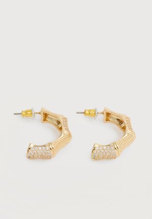 Øreringe i guldfarvet bambusform med små klare krystaller på den nederste halvdel og lukning med stiftbag.