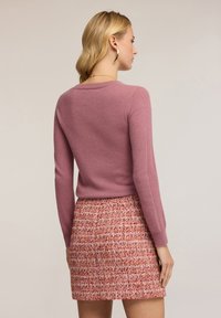 Maglione aderente rosa chiaro con maniche lunghe, abbinato a una gonna in tweed strutturata e multicolore in tonalità di rosso e rosa.