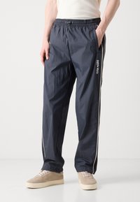 Marineblauwe trackpants van lichtgewicht, gestructureerd materiaal, met witte zijkanten en een elastische tailleband met een koord.