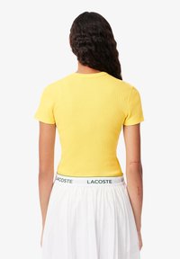 Geel aansluitend T-shirt met een ribbelstructuur, korte mouwen en een ronde hals, gedragen met een witte rok met een groene merkband.