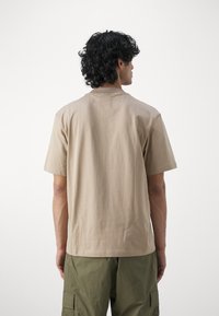 Kortærmet, beige bomuld t-shirt med rund halsudskæring, der har en glat tekstur og en afslappet pasform. Bagsiden viser en ensfarvet design.