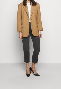 Blazer de gran tamaño color marrón con dos botones, combinado con pantalones cortos vaqueros oscuros. Zapatos de tacón alto negros completan el conjunto.
