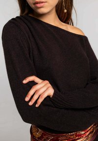 Jersey negro de punto con un diseño de hombros al descubierto, puños acanalados y una textura suave. Combinado con una tela colorida y estampada en la cintura.