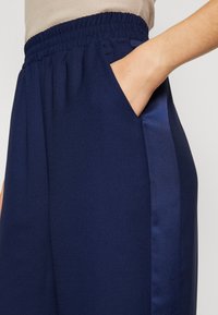 Pantalon bleu marine en tissu doux, avec une ceinture élastique, une poche latérale et un détail de bande latérale semblable à du satin.