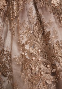 Intricate gold lace fabric featuring floral patterns, embellished with small pearls and beads, highlighting a sheer, textured surface.