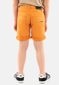 Shorts in denim arancione con risvolti, dotati di due tasche posteriori e un'etichetta nera in vita. Abbinati a sneakers nere.