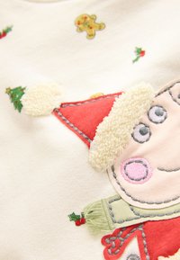 Tissu en coton blanc avec un motif coloré brodé comprenant un bonnet de Père Noël, un bonhomme en pain d'épices et des sapins de Noël aux couleurs variées.