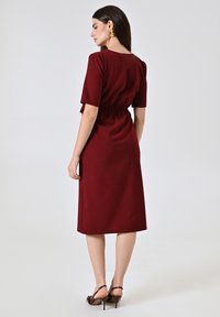Robe bordeaux à manches courtes, taille cintrée et ourlet droit, en tissu texturé. Sandales à talons bruns complètent le look.