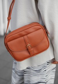 Borsa a tracolla in pelle marrone con finitura testurizzata, dotata di una patta anteriore, dettaglio con fibbia e chiusura con zip. Include una tracolla regolabile.