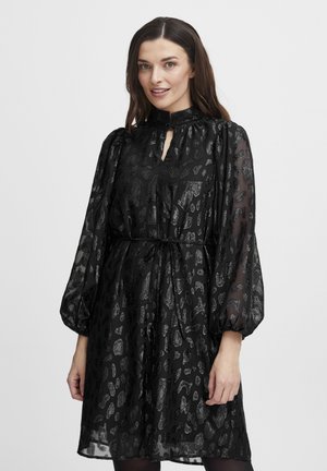 Rochie neagră dintr-un material transparent, texturat, cu un imprimeu animalier subtil. Gât înalt, detaliu cu tăietură în formă de cheie și mâneci bufante, cu un cordon la talie.