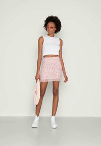 Top cropped branco e saia mini rosa com padrão floral. Ténis brancos e uma bolsa rosa clara completam o visual. Texturas suaves, design ajustado.