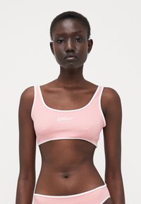 Lys rosa sports-bh med hvit trim og 'Hilfiger'-logo i midten. Glatt stoff, tettsittende design, firkantet utringning.