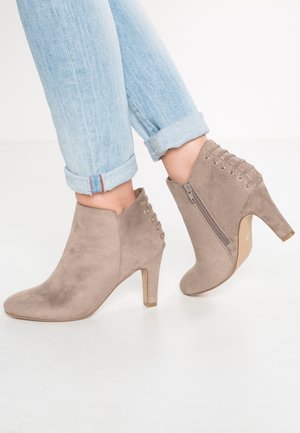 Pieds vêtus d’un jean bleu clair retroussé et de bottines en daim taupe avec des fermetures éclair latérales et des talons carrés.