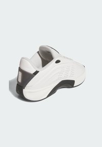 Vit sneaker med ett slätt syntetiskt ovandel, svarta accenter, en texturerad häl och perforerade detaljer på sidan för andningsförmåga.