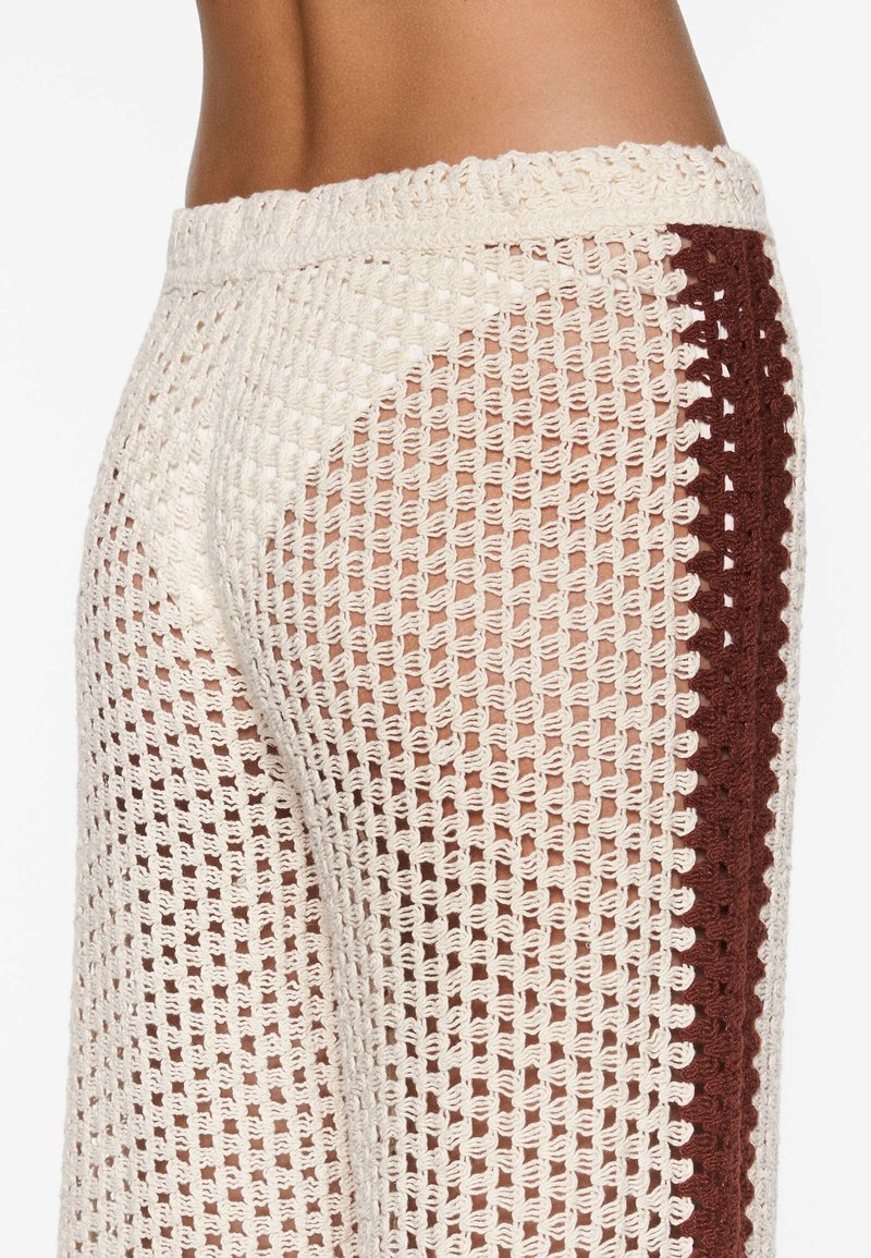 Pantaloni leggeri in maglia aperta color crema con una striscia laterale bordeaux. Caratterizzati da un design in crochet texturizzato e una fascia in vita larga per il massimo comfort.