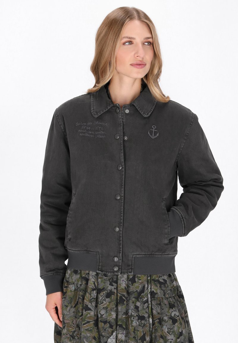 Fekete farmerdzseki galléros nyakkivágással, elöl gombos rögzítéssel és hímzett horgony részlettel. Hosszú ujja van és bordás mandzsettákkal rendelkezik.