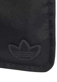 Černá texturovaná taštička vyrobená z odolné tkaniny, se způsobeným černým embosovaným logem ve tvaru tří listů. Okraje jsou prošité pro zvýšení pevnosti.