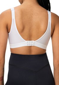 Top sportivo bianco con spalline regolabili, design a schiena bassa e chiusura a gancio con quattro file di ganci. Leggings neri a vita alta.