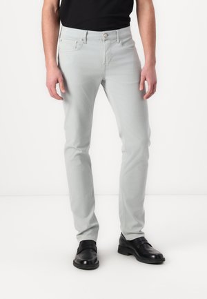Jeans slim-fit de culoare gri deschis, cu buzunare frontale, închidere cu nasture și o textură netedă. Purtați cu pantofi de birou negri și o cămașă neagră.