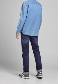 Camisa de mezclilla azul claro, jeans azul oscuro y zapatillas verdes con acentos blancos. La camisa tiene mangas largas y cuello abotonado.