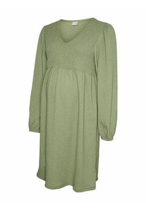 Robe de maternité verte avec un décolleté en V, un corsage froncé, des manches longues bouffantes et une jupe fluide, confectionnée dans un tissu texturé.