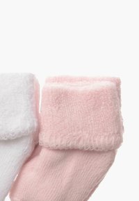 Ein Paar Babysocken aus weichem, weißem und pinkem Baumwollmaterial, mit plüschigen, gerippten Bündchen und einer glatten Textur. Jede Socke hat eine abgerundete Form.