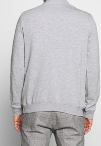 Sweat-shirt gris avec un col rond et des poignets côtelés, présentant une texture lisse et une coupe décontractée, assorti à un pantalon à carreaux.