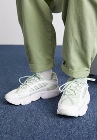 Vita och mintgröna sneakers med meshdetaljer, rund tå, tjock sula och strukturerade accenter, kombinerade med uppvikta ljusgröna byxor.