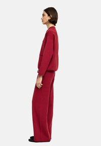 Czerwony, przerośnięty sweter z dzianiny z boczną kieszenią, w połączeniu z szerokimi spodniami, wszystko w dopasowanym kolorze, o luźnym kroju.