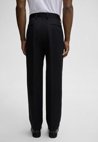 Schwarze, taillierte Hose mit geradem Schnitt, zwei Gesäßtaschen, glatter Textur und einem Bund mit Gürtelschlaufen.