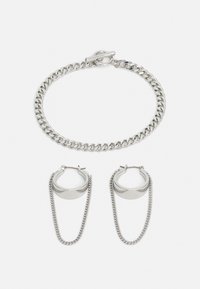 Silberne Kettenarmband mit Drehverschluss und passenden Creolen, die eine Kettendetail an der Unterseite aufweisen. Schlanker, metallischer Finish.