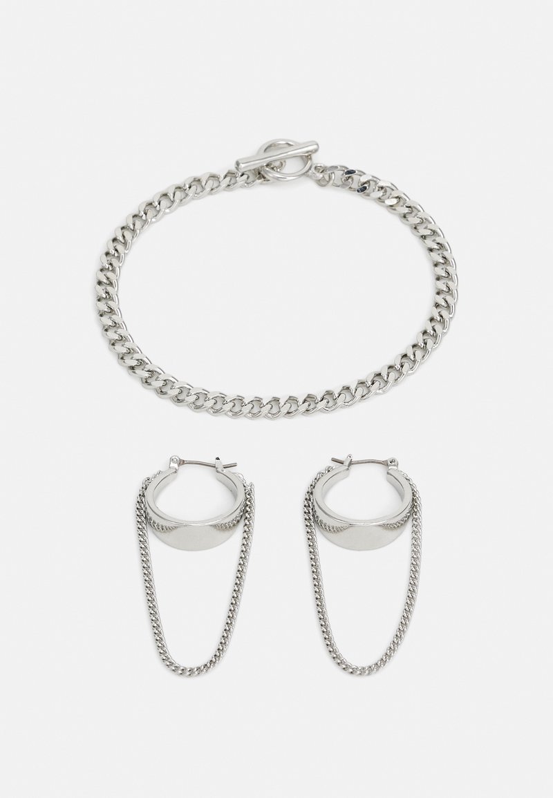 Silberne Kettenarmband mit Drehverschluss und passenden Creolen, die eine Kettendetail an der Unterseite aufweisen. Schlanker, metallischer Finish.