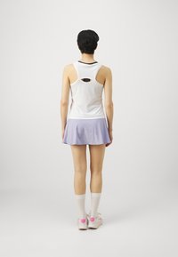 Top blanco sin mangas con detalle de corte, combinado con una falda acampanada lila. La modelo lleva calcetines blancos y zapatillas ligeras con acentos rosas.