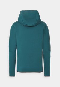 Teal långärmad hoodie med svart kant vid ärmsluten och nederkant, visad bakifrån mot en vit bakgrund.