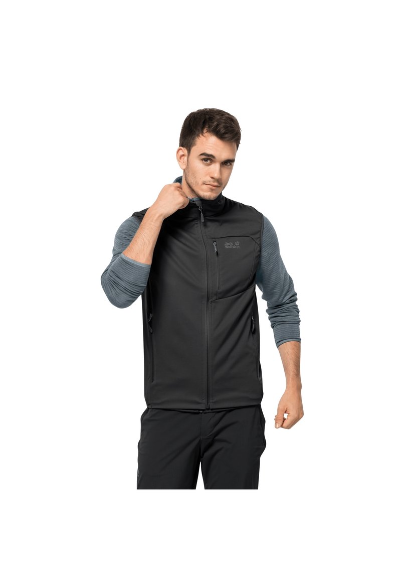 Black softshell vest with front zip, side pockets, and a logo. Worn over a gray long-sleeve shirt. Suitable for outdoor activities.