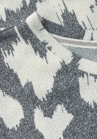 Pull en tricot avec un motif abstrait gris clair et gris foncé, col rond et tissu texturé pour une sensation cocooning.