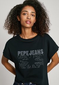 Juodas medvilnės marškinėliai trumpomis rankovėmis, papuošti tekstūruotu cirkonių dizainu, kuris užrašytas "PEPE JEANS" skirtingomis šrifto rūšimis ir dydžiais.