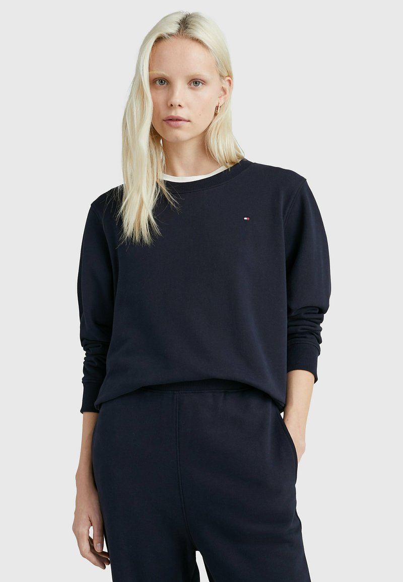 Felpa blu navy con maniche lunghe e collo rotondo. Realizzata in tessuto morbido, presenta un logo discreto sul petto. Abbinata a pantaloni della tuta coordinati.