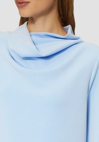 Lichtblauw gedrapeerde top met een zachte, gladde textuur en een cowl halslijn. Het ontwerp heeft zachte plooien en een relaxte pasvorm.